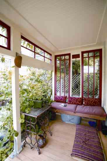 Radiant coral-red trim and red and pink pillows on Alma Hecht’s front porch bench welcome visitors, creating one of many small seating or outdoor entertaining spaces around her San Francisco cottage.